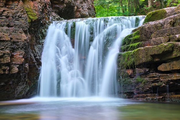 Cachoeira no rio da montanha com água espumosa branca caindo de formação rochosa na floresta de verão.