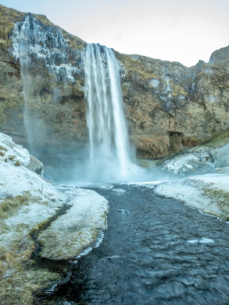 Foto cachoeira siljalandsfoss na islândia grande cachoeira com penhasco natural com neve e gelo ao redor