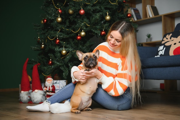 Cachorrinho com dono brincando e se divertindo jovem adolescente sentada no sofá com sua árvore de Natal de estimação ao fundo foco seletivo suave