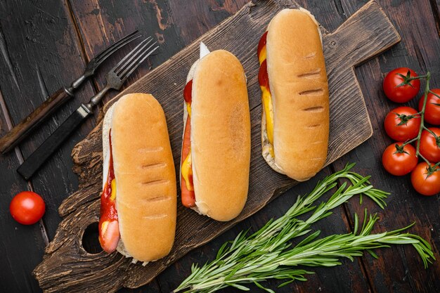 Cachorro-quente com ketchup e mostarda amarela na velha mesa de madeira escura vista superior plana