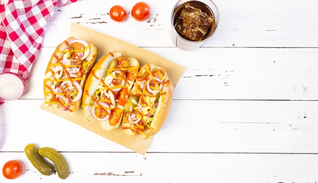 Cachorro-quente com vegetais, mostarda e ketchup em uma tábua de cortar em uma mesa de madeira branca, vista de cima, copyspace