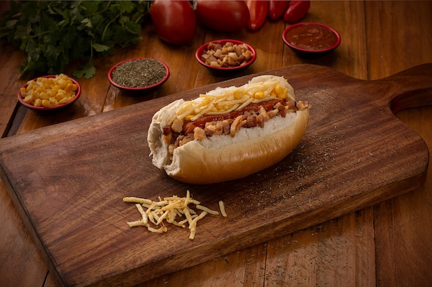 Cachorro-quente em uma placa de madeira cercado por temperos e vegetais, como tomates, pimentões e cebolas