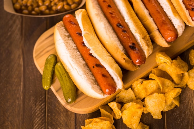 Cachorro-quente grelhado com pãezinhos de cachorro-quente branco com batatas fritas e feijão cozido ao lado.