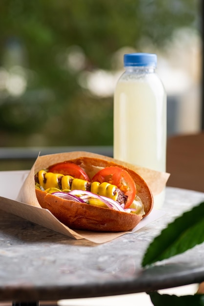 Cachorro-quente tradicional com salsicha defumada em um rolo fresco guarnecido com mostarda e servido com alface tomate e cebola em um fundo de pedra cinza