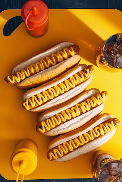 Foto cachorros-quentes grelhados de churrasco com mostarda americana amarela sobre fundo escuro de madeira
