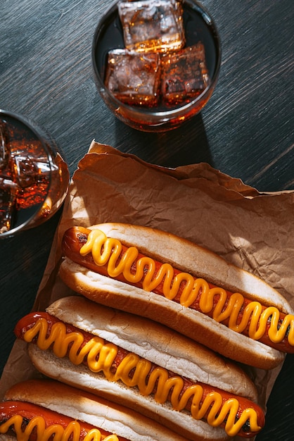 Cachorros-quentes grelhados de churrasco com mostarda americana amarela sobre fundo escuro de madeira