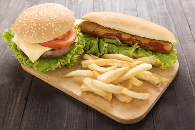 Cachorros-quentes, hambúrgueres e batatas fritas na madeira