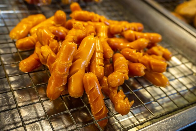 Cachorros-quentes ou salsichas fritos em óleo numa grelha de aço inoxidável