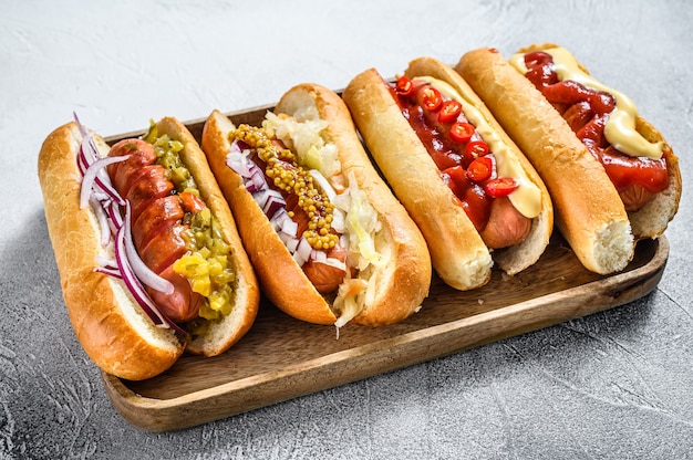 Cachorros-quentes totalmente carregados com coberturas variadas em uma bandeja.