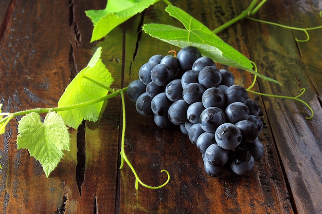 Cachos de uvas frescas com ramos e folhas na mesa de madeira rústica, close-up