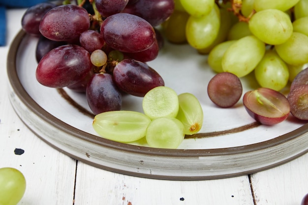 Cachos de uvas verdes e vermelhas maduras frescas em uma mesa de madeira