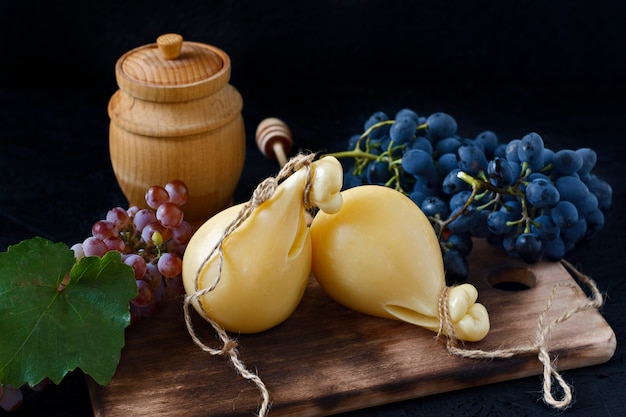 Caciocavallo do queijo em uma placa de madeira com uvas e mel em um fundo preto. Pêra de queijo