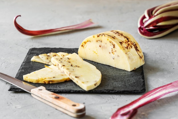 Caciotta de queso blando tradicional italiano con radicchio cortado en tablero de piedra de fondo gris y rosa