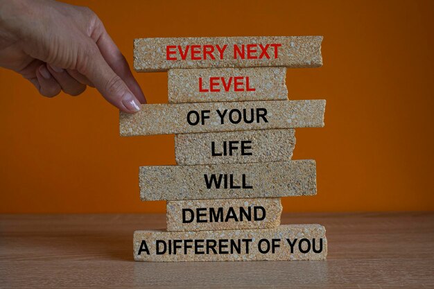 Cada siguiente nivel de tu vida requerirá un tú diferente. Palabras rojas en bloques de ladrillo.