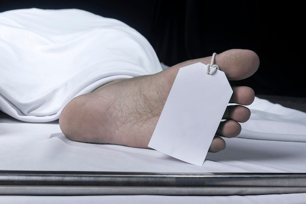 Cadáver humano cubierto con una sábana y una etiqueta con el nombre en la morgue