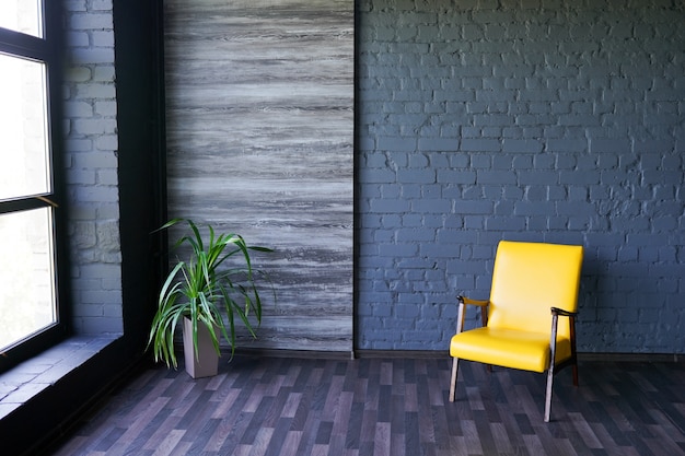Cadeira amarela perto da janela no interior escuro moderno com parede de tijolo preto, cópia espaço