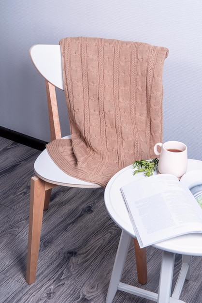 Cadeira branca e um suporte de mesa na sala Há uma manta de malha bege na mesa. copo de chá