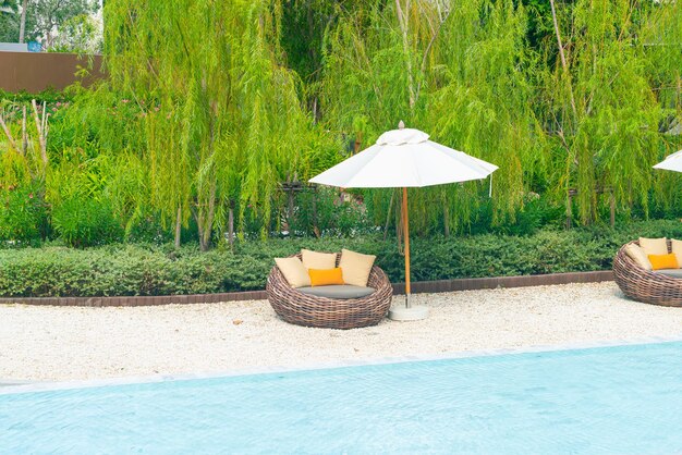 cadeira de pátio ao ar livre com travesseiro e guarda-chuva ao redor da piscina - feriados e conceito de férias