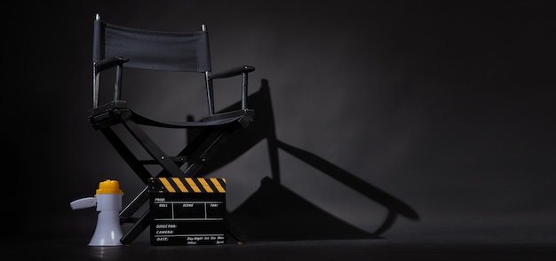 Cadeira do diretor preta e claquete ou claquete de cinema com megafone em fundo preto. Use na produção de vídeo ou na indústria do cinema cinematográfico