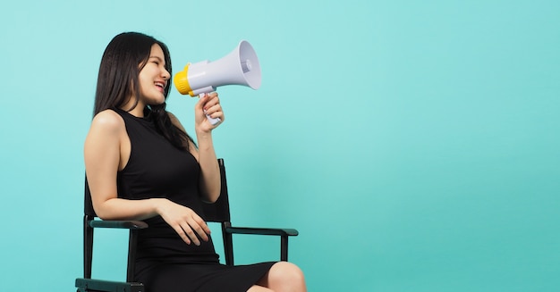 Cadeira preta do diretor e uma mulher asiática estão sentadas nela. Ela segura o megafone na cor hortelã ou no fundo azul Tiffany.