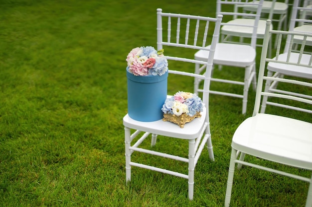 Cadeiras Chiavari na grama Em uma das cadeiras há uma caixa de chapéu com flores Clouseup
