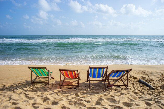 Cadeiras coloridas na praia com sol do verão, água do mar clara e o céu azul.