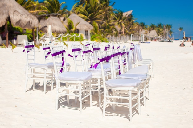 Cadeiras de casamento branco decoradas com arcos roxos na praia