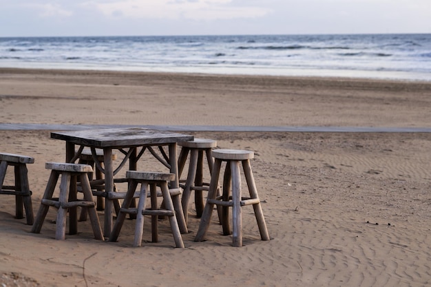 Cadeiras de madeira e uma mesa em uma ampla praia de areia com uma costa em perspectiva
