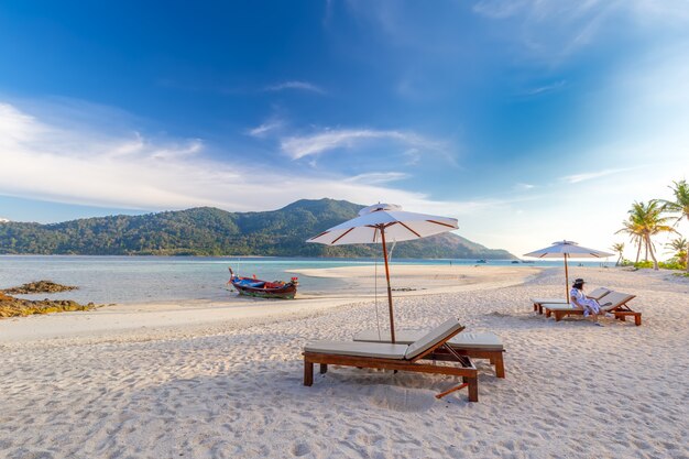 Cadeiras de praia, guarda-chuva e palmas das mãos na bela praia para férias e relaxamento na ilha de Koh Lipe, Tailândia