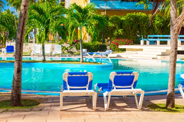 Cadeiras de praia perto da piscina em resort tropical com palmeiras.