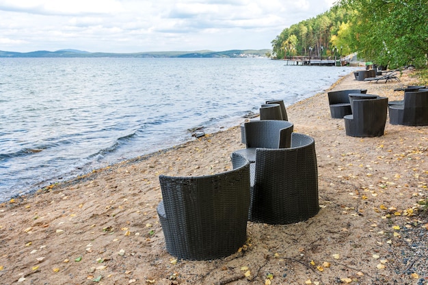 Cadeiras vazias ficam na costa de um lago de montanha em um dia nublado de outono