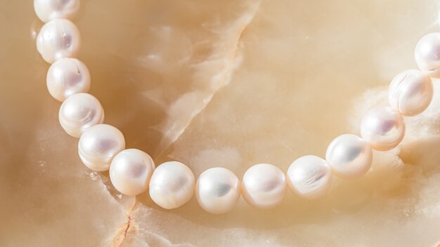 Cadena de perlas blancas de la naturaleza sobre fondo de mármol en enfoque suave, con reflejos.