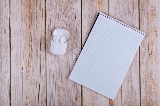 Caderno aberto com fones de ouvido sem fio na mesa de madeira