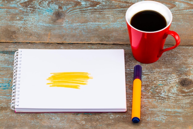 Foto caderno aberto com listras de marca-texto amarelas desenhadas à mão e xícara de café na mesa de madeira.