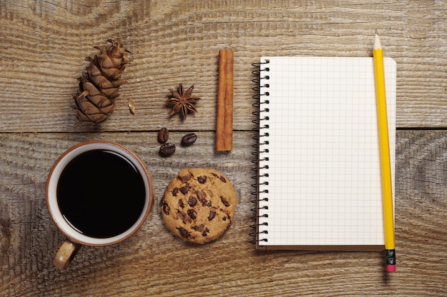 Caderno aberto e xícara de café quente com saborosos biscoitos de chocolate na velha mesa de madeira. Vista do topo