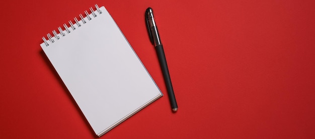 Foto caderno aberto em uma mola e uma caneta esferográfica preta em uma cópia de fundo vermelho