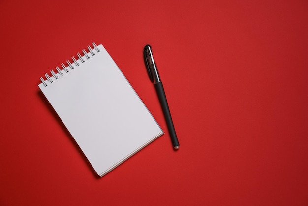 Caderno aberto em uma mola e uma caneta esferográfica preta em uma cópia de fundo vermelho