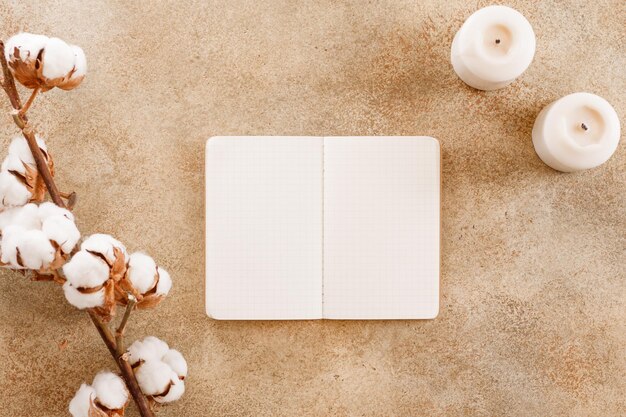 Caderno aberto entre galho de flores de algodão e velas brancas em um fundo de pedra bege texturizado Espaço de cópia de vista superior plana