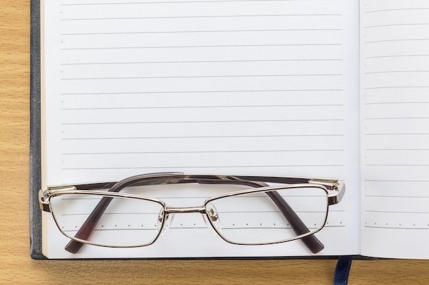 Caderno aberto página em branco e óculos