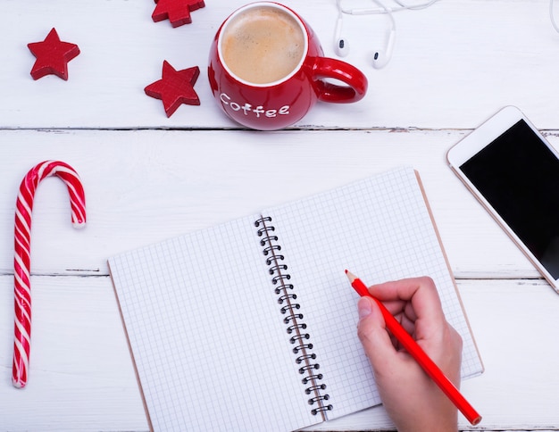 Caderno aberto vazio e mão feminina com um lápis de madeira vermelho