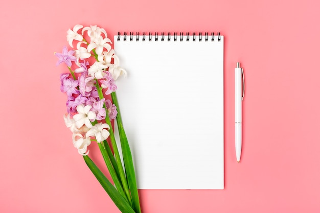 Caderno branco aberto, caneta, buquê de flores jacintos em fundo rosa