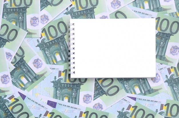 Foto caderno branco com páginas limpas sobre um conjunto de denominações monetárias verdes de 100 euros