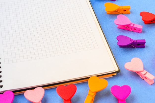 Caderno branco para notas e muitos corações em um fundo azul.