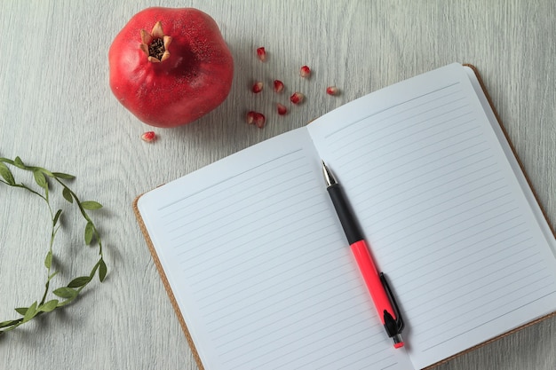 Caderno, caneta e romã na mesa