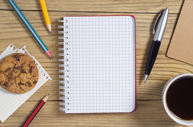 Caderno, caneta, lápis e café com biscoitos na mesa, vista superior