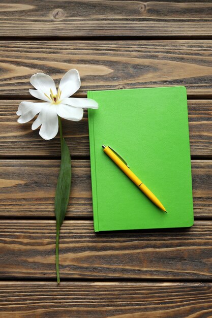 Foto caderno com caneta e tulipa branca em fundo de madeira