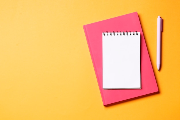 Caderno com caneta em um fundo laranja.