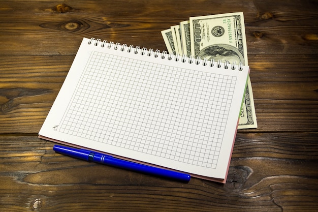 Foto caderno com caneta esferográfica e notas de dólar na mesa de madeira. conceito de economia de dinheiro