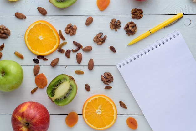 Caderno com caneta rodeado de maçãs, kiwi, frutas secas, laranjas e maçãs. O conceito de uma dieta saudável e lista de compras.