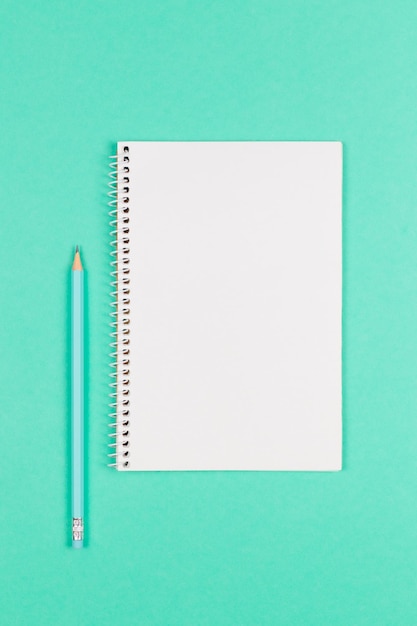 Caderno com página em branco e lápis em fundo turquesa